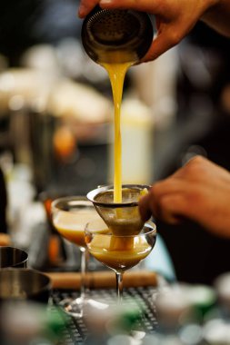Bir barmen taze kokteyl karışımını ince bir ağ süzgecinden geçirip coupe bardağına koyar..