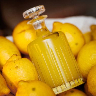 Limoncello dolu bir cam şişe bütün limonların arasında duruyor. Parlak sarı tonlar tazeliği ve narenciyeyi vurgular..