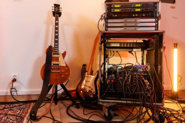 İki elektro gitar ses ekipmanlarının yanında duruyor ve kayıt stüdyosunun zemininde birbirine dolanmış kablolar..
