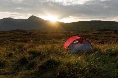 Güneş uzak tepelerin ardında batarken çimenli bir dağ vadisinde tek bir kırmızı çadır duruyor..