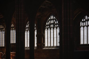 Büyük kavisli pencereleri ve süslemeli taş mimarisi olan tarihi Gotik katedralin iç manzarası. Yumuşak gün ışığı desenli camdan içeri girer ve karanlık iç mekanı aydınlatır..