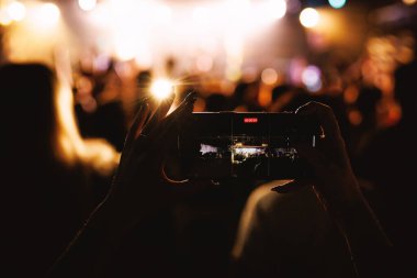 Akıllı telefon ekranı, parlak ışıklarla bir konser kaydediyor. Kalabalığın siluetlerini oluşturuyor..