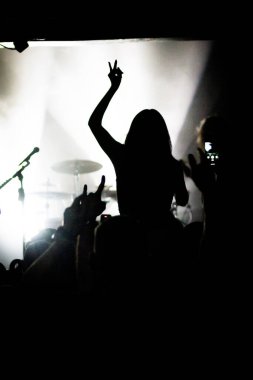 Coşkulu kalabalık, parlak sarı bir konser sahnesinin önünde el kaldırıyor..