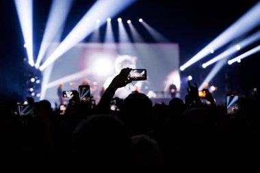 Kalabalığın arkasından bakıldığında, göstericileri filme almak için gösterilen çok sayıda parlayan telefon ekranı görülüyor. Karanlığın içinden geçen dramatik mavi ve beyaz ışık huzmeleri..