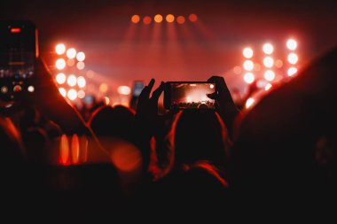 Çoklu hayranlar, parlak ekranlı akıllı telefonları, parlak kırmızı ışık altında sahneye çıkan bir grubu kaydetmek için tutuyor..