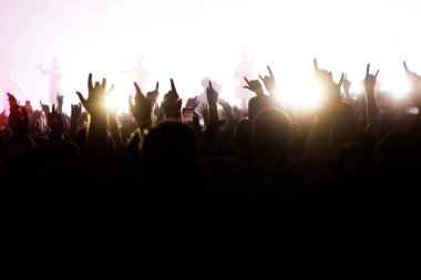 İzleyiciler bir festivalde parlak beyaz bir sahneye rock 'n roll el hareketi yapıyorlar..