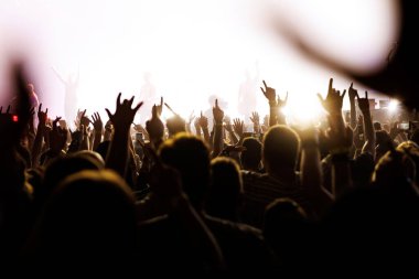 Hayranlar, performans sırasında yoğun beyaz sahne ışıklandırması zeminine karşı rock hareketleri yaparlar. Kalabalık siluette görünüyor..