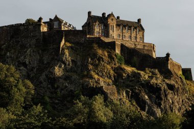 Tarihi Edinburgh Kalesi 'nin alçak açılı manzarası volkanik bir uçurumun tepesine tünemişti. Eski taş duvarlar, batan güneşin sıcak ışığıyla aydınlanır..