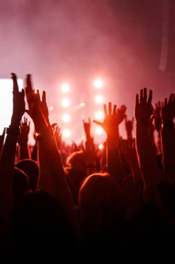 Kırmızı ışık ve sisle dolu bir müzik performansı sırasında kalabalık bir hayran kitlesi kollarını parlak bir sahneye kaldırıyor..