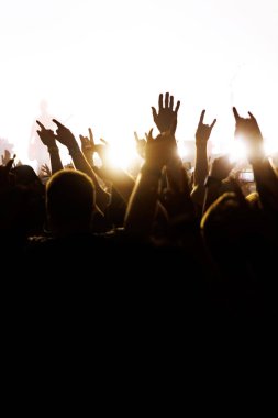 Parlak sahne ışıkları tezahürat yapan bir kalabalığı aydınlatıyor. Açık hava müzik etkinliğinde ağır metal el hareketleri yapıyorlar..