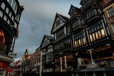 Siyah-beyaz Tudor tarzı mimari, geleneksel dükkanlar ve kapalı yürüyüş yollarıyla Chester caddelerini kaplıyor..