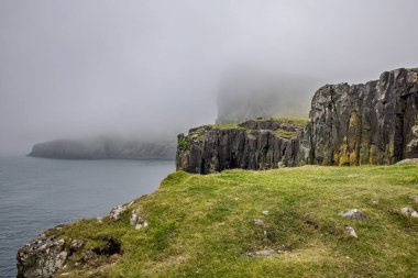 Dramatik kayalık kayalıklar karanlık okyanus suyuna düşer. Tepeleri kalın ve kasvetli sislerle gizlidir. Engebeli İskoç kıyı şeridi vahşi ve el değmemiş bir doğa hissi veriyor..