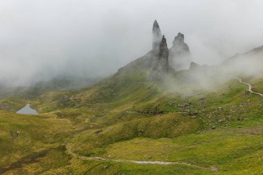 Yüksek bir manzara bir iz ve Storr 'un sisli kayalıklarının altındaki yeşil tepelerin arasına yerleştirilmiş küçük bir lochan gösteriyor..