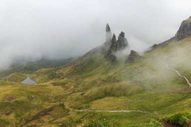 Dağlık İskoçya 'da sisli bir günde yeşil bir vadiden kayalık tepelere ve küçük bir göle uzanan toprak bir patika..