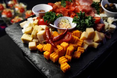 Mavi peynir, çedar, salam ve biber de dahil olmak üzere çeşitli gurme aperatifler koyu bir taş tabakta servis edilir..