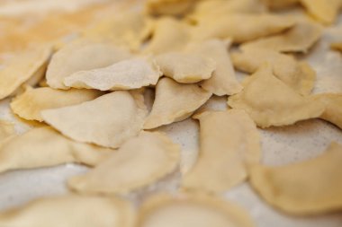 Pişmemiş hamur köftesi yığını, muhtemelen pierogi, beyaz unlu bir masada oturuyor. Hamur köfteleri kıvrımlı kenarlarıyla hilal şeklinde, kaynamaya hazır..