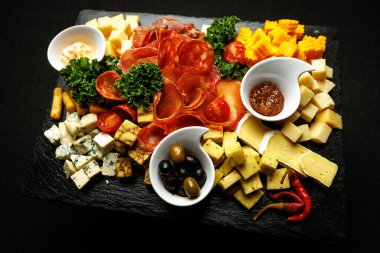 Üzerine dilimlenmiş salam, jambon, küp peynir, zeytin ve küçük kaseler dolusu sos serpiştirilmiş koyu bir levha. Taze yeşiller garnitür olarak kullanılır..