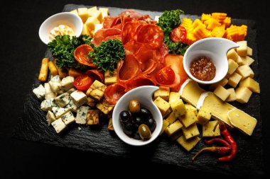 Koyu taş servis tahtasına yerleştirilmiş çeşitli aperatiflerin genel görünümü.