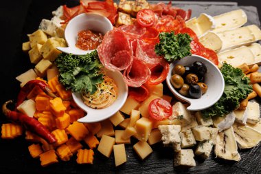 Bir tepside sunulan çeşitli pişmiş etler, sert ve yumuşak peynirler ve sebze süsleri..