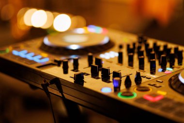 Ilık ortam ışıkları altında ışıklı düğmeleri ve düğmeleri olan modern bir DJ destesini kapat.