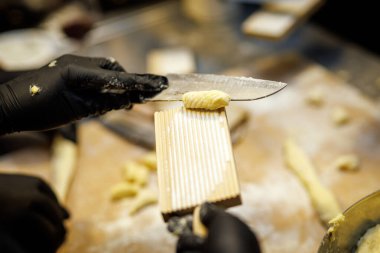 Makarna hamurunu şekillendirmek için bıçak ve tırtıklı tahta kullanan profesyonel bir aşçı..