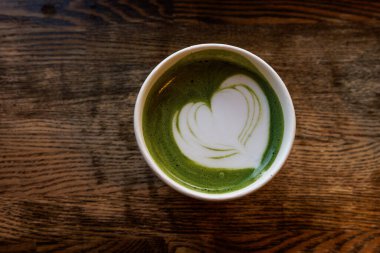 Parlak yeşil kibrit latte dolu bir kağıt bardak koyu ahşap bir masada oturur..