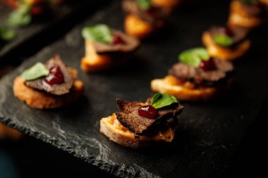 İnce dilimlenmiş sığır eti, tatlı böğürtlen reçeli ve taze yeşil yapraklı küçük ekmek yuvarlaklarına odaklanın..