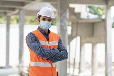 Erkek mühendis COVID 19 'un konut projesindeki inşaat projesine güveni tam olmasını önlemek için maske takıyor. 