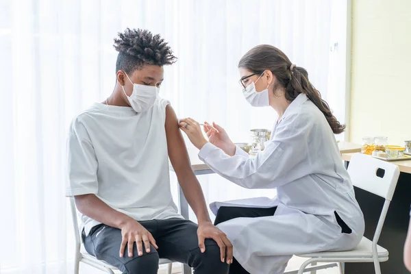Maske takan ve yüz maskesi takan bir doktor, bir Afrikalı Amerikalının koluna aşı yapılan bir adamı COVID-19 'a yakalanmaktan korumak için aşı şırıngası tutuyor.. 