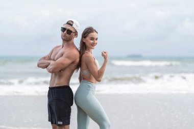 Spor kıyafetleri giyen güzel beyaz kadın denizin kumlu sahilinde dalgalarla birlikte iki ayak yükselterek yoga yapıyor. Spor, egzersiz ve sağlık konsepti.