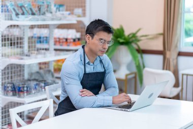 Marketi olan erkek küçük işletme sahibi bir mağazada önlük takıyor, envanter kontrolü yapıyor, hesap bakiyelerini kontrol ediyor ve internetten sipariş alıyor.. 