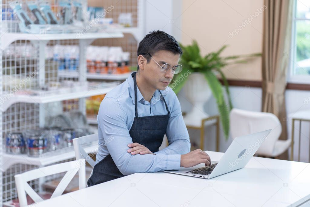 Male small-business owner who owns a grocery store wears a apron in a store, checks inventory, check account balances, and get order online business. 