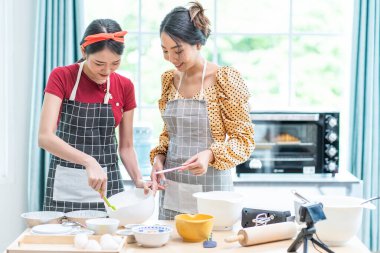 Güzel bir Asyalı kadın yemek yapmayı sever ve başka bir kız arkadaş da evdeki mutfağın fırınında turta tavası tutar..