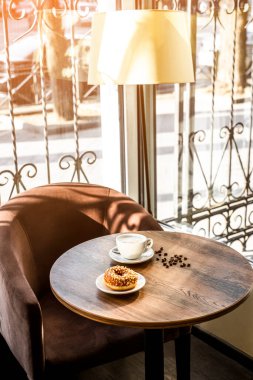 wooden table with an armchair and a floor lamp. cappuccino, donut on a wooden table close-up. lunch break in a cafe