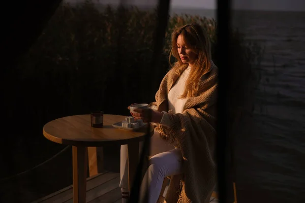 beautiful young girl drinks tea in nature by the lake. a woman is resting in a glamping in a picturesque location far from the city. self-isolation vacation without people