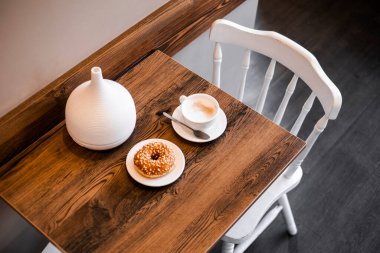 Kahve ve tatlı ahşap bir masada. Masanın arka planında iki beyaz sandalye var. Kahvaltı için rahat bir yer.