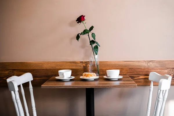 rose, coffee and dessert on a wooden table. table with two white chairs on a light background side view. cozy place for a date. Valentine\'s Day