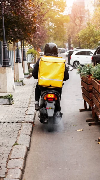 Yemek teslimatı kuryesi bir müşterinin evine motosikletle sipariş veriyor. Karantina sırasında paket yemek. Paketlerin eve teslimatı. Büyük bir sırt çantası olan motosikletli.