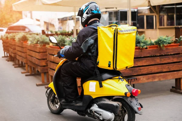 A food delivery courier is driving an order to a customer\'s home on a moped. takeaway food during quarantine. transport delivery of parcels at home. motorcycle rider with a big backpack