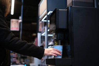 Adam kendine self-servis makinesinde kahve yapıyor. Kapuçino dükkandaki kasada duruyor. Süpermarkette kahve makinası. izolasyon 2020
