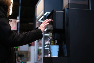 Adam kendine self-servis makinesinde kahve yapıyor. Kapuçino dükkandaki kasada duruyor. Süpermarkette kahve makinası. izolasyon 2020