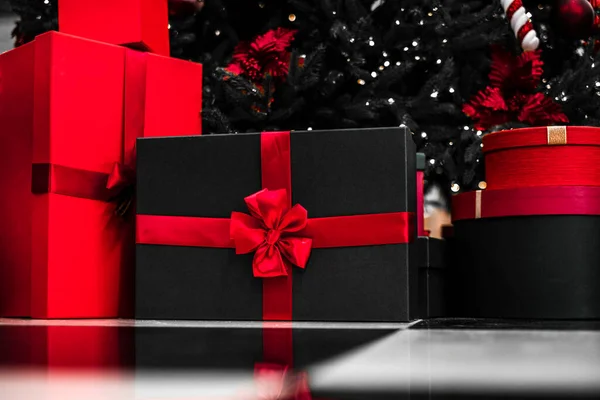 gift black boxes with red ribbon are beautifully packaged andlie under the Christmas tree. boxes with surprises from santa claus under the tree. christmas and happy new year