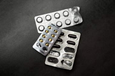 Koyu gri bir masanın üzerinde açık ilaç kabarcıkları var. Coronavirus için haplar, soğuk algınlığı için ilaçlar. Kapsüllerde vitaminler. Yukarıdan görünüm