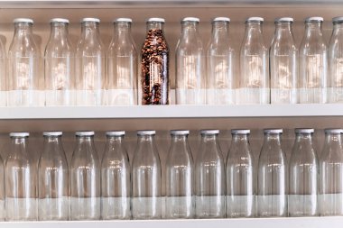 Son kahve çekirdeği şişesi diğer boş cam şişelerin yanında bir rafta duruyor. makro fotoğraf. Depolama için konteynırda tahıl kahvesi. Canlandırıcı organik içecekler. kahve üretim ve depolama