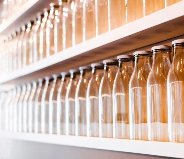 a lot of empty glass bottles with a white cap are on the shelf in a row. bottle for storing milk, juice, drinks and more. glass jar on a shelf in the kitchen. bottle production