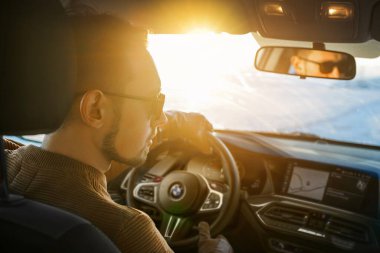 Güneş gözlüklü genç yakışıklı bir adam BMW arabasıyla İzlanda 'nın altın yüzüğüne biniyor. Avrupa 'yı arabayla dolaşmak. Arabadaki bir adamın portresi. İzlanda, Vik Aralık 2020                  