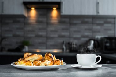 Mutfak masasında bir tabak kruvasan olan bir fincan çay. Tatlı tarafı manzaralı. Şekerli sabah kahvesi. Yemek tarifi. Çikolatalı kruvasan. Fransız yemeği.