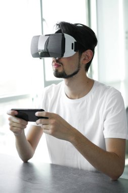 Genç adam evde VR gözlük takarak sanal gerçeklik oyunu oynuyor. Çoklu oyuncu oyunu. Çevrimiçi oyunlar. Yayınlanan video oyunları. Adam video oyunları oynuyor. Biraz rahatla. Neşeli hafta sonu. 