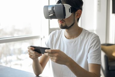Genç adam evde VR gözlük takarak sanal gerçeklik oyunu oynuyor. Çoklu oyuncu oyunu. Çevrimiçi oyunlar. Yayınlanan video oyunları. Adam video oyunları oynuyor. Biraz rahatla. Neşeli hafta sonu. 