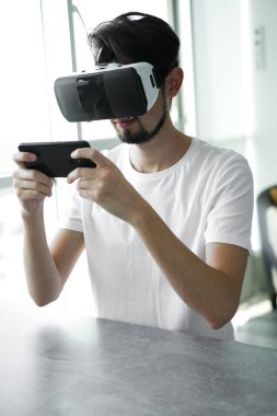 Genç adam evde VR gözlük takarak sanal gerçeklik oyunu oynuyor. Çoklu oyuncu oyunu. Çevrimiçi oyunlar. Yayınlanan video oyunları. Adam video oyunları oynuyor. Biraz rahatla. Neşeli hafta sonu. 